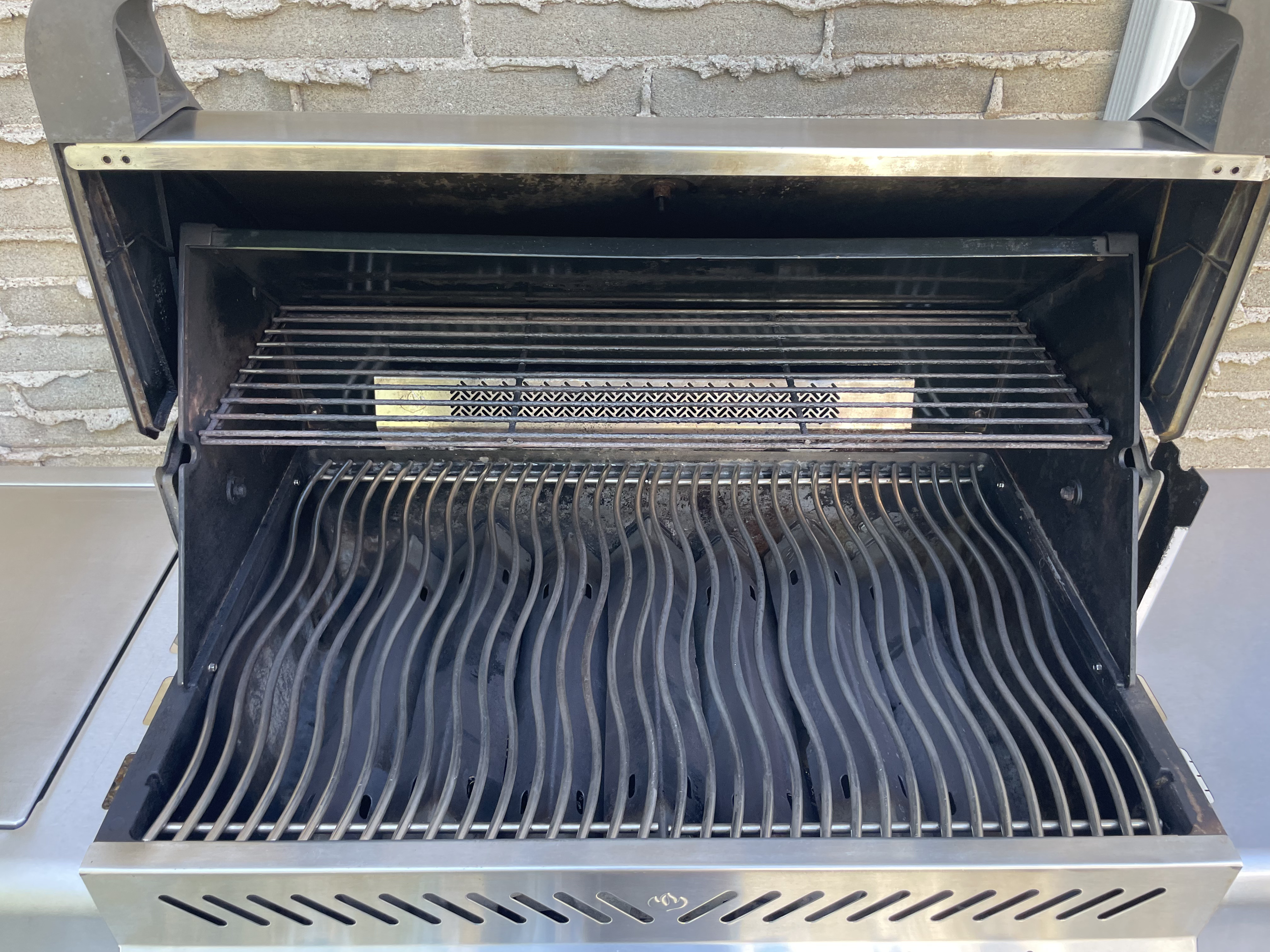 Inside the same Napoleon Prestige after an Aspect deep clean, with degreased wavy cooking grates, a clean warming rack and a soot-free lid and firebox