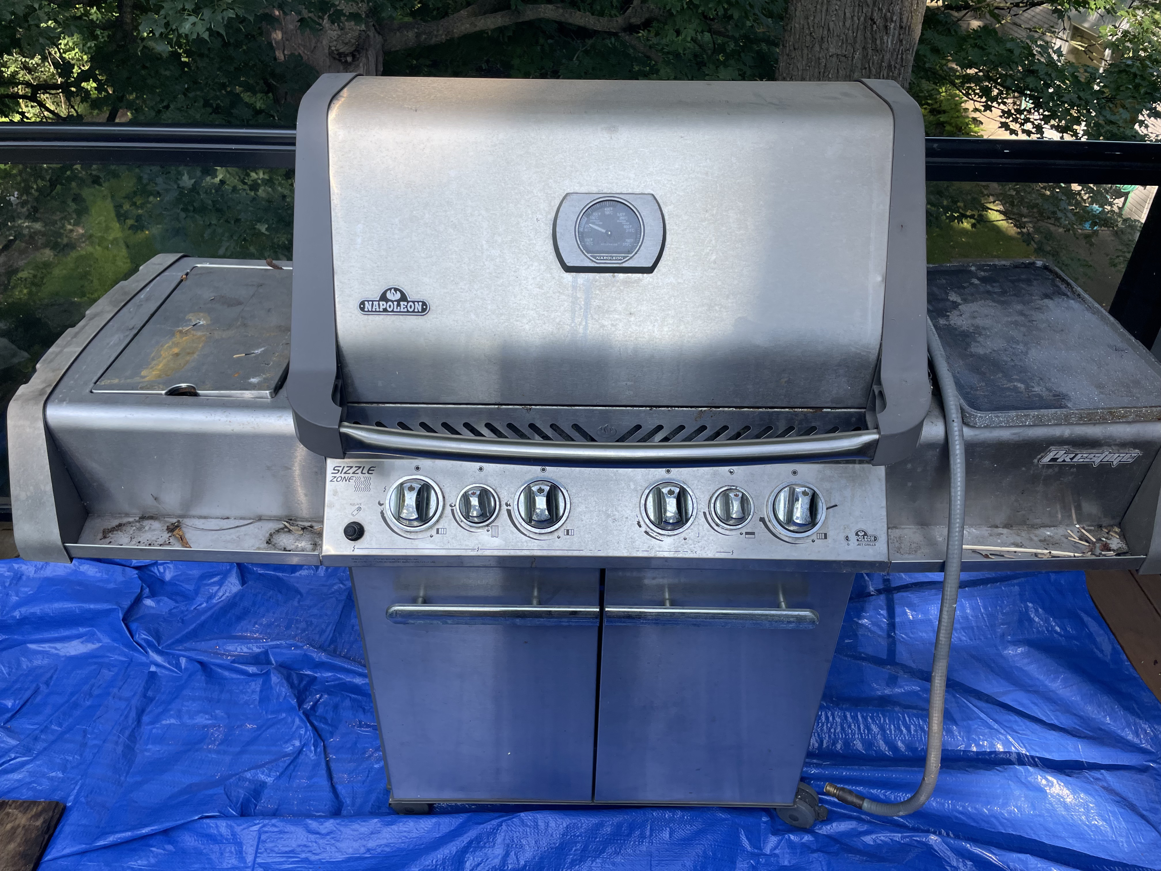 The same second Napoleon Prestige standing on a work tarp before an Aspect deep clean, its stainless lid and side shelves smeared with grease and dirt