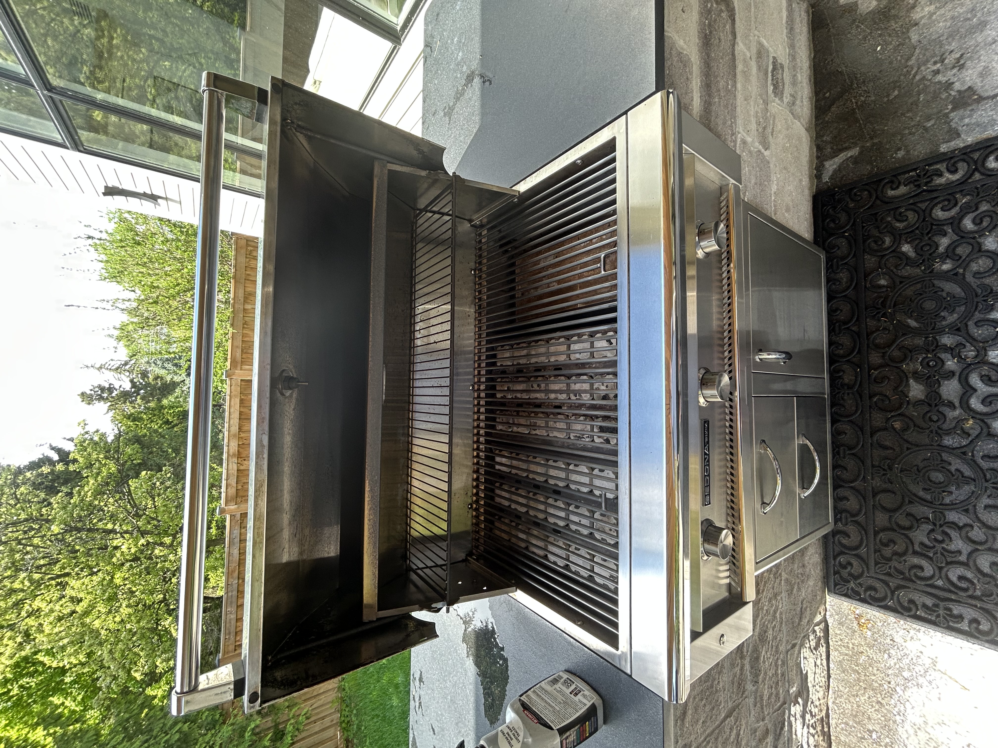 The same Sedona by Lynx grill after an Aspect deep clean, open on a stone patio with clean grates, a clear warming rack and a polished stainless cart