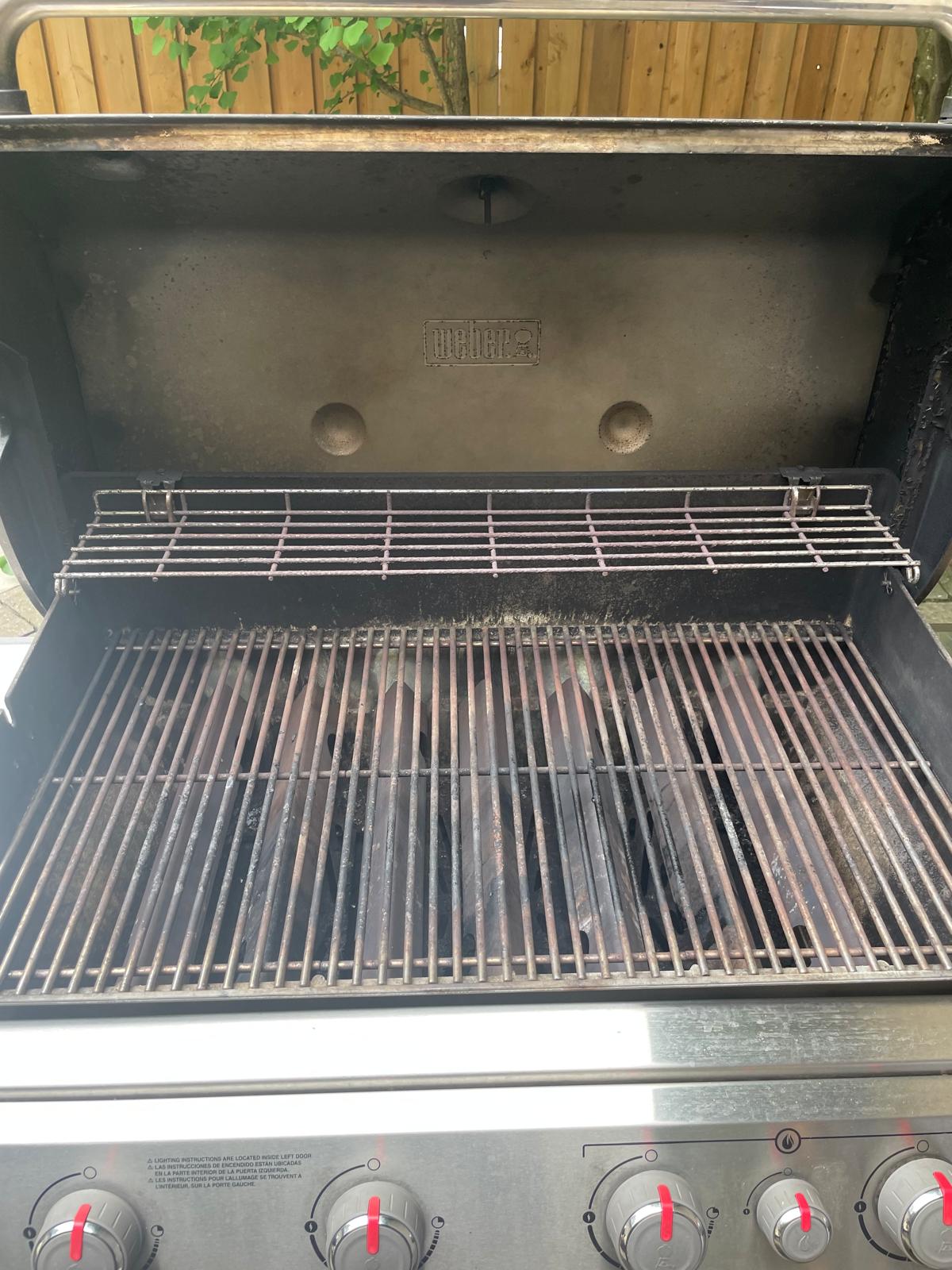 Inside a second four-burner Weber Genesis before an Aspect deep clean, its grates greyed with baked-on grease under a smoke-stained lid